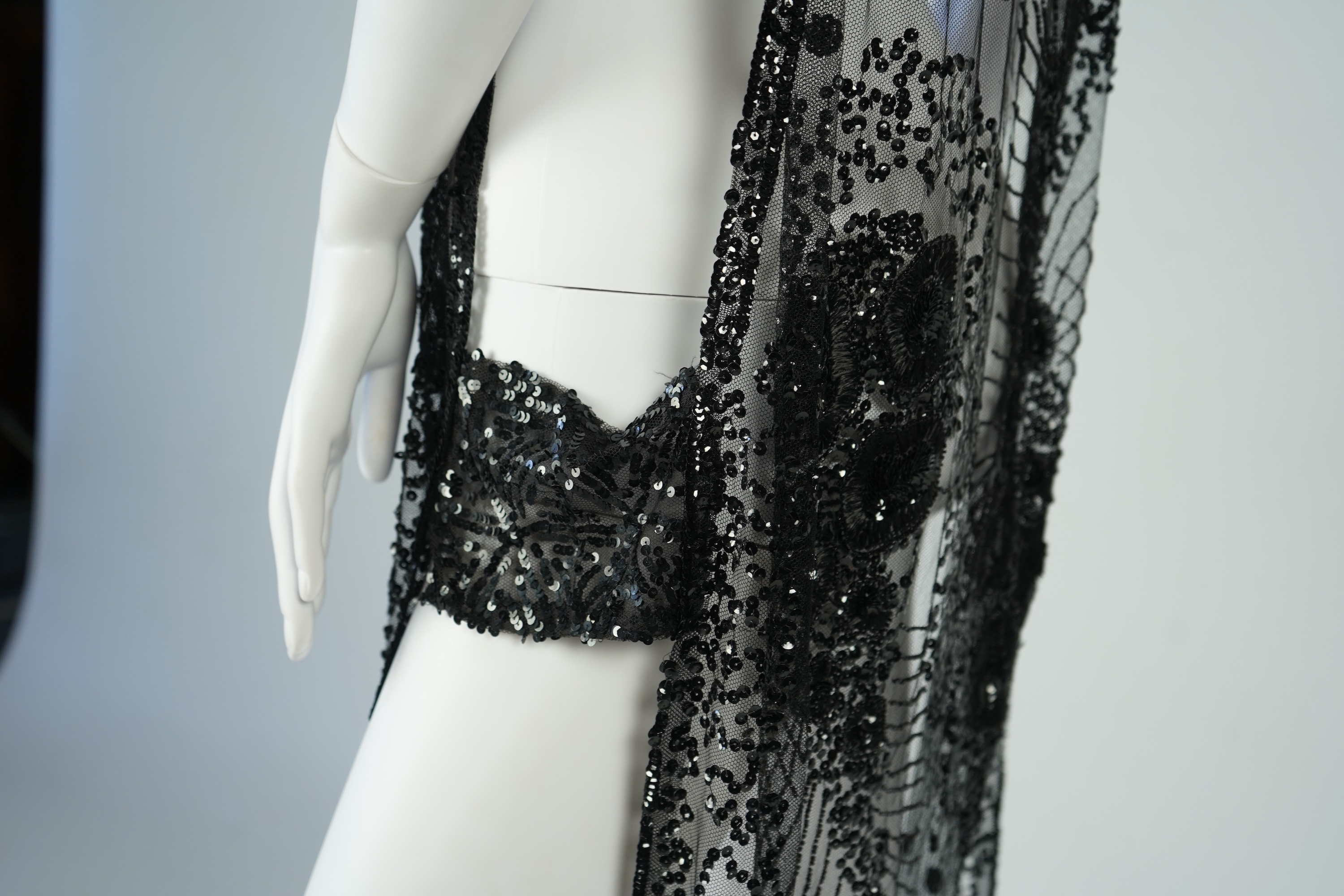 A 1920's black sequin on net tabard, with floral decoration and two side sequinned straps. Length 97cm. Condition - a few sequins have detached but are in a bag for re-attaching.
